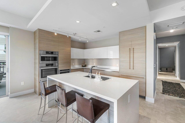 kitchen featuring white cabinetry, a kitchen island with sink, a breakfast bar area, double oven, and sink