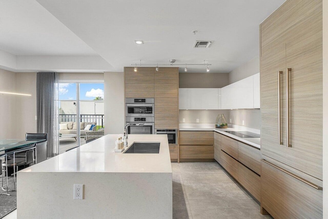 kitchen with an island with sink, white cabinetry, double oven, and black electric cooktop