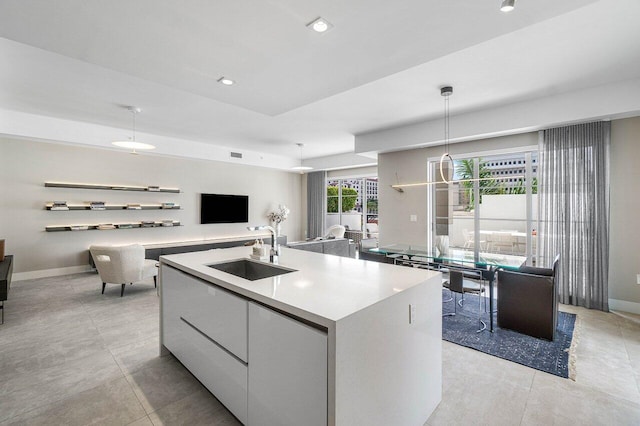 kitchen with pendant lighting, light tile patterned flooring, a kitchen island with sink, sink, and white cabinetry