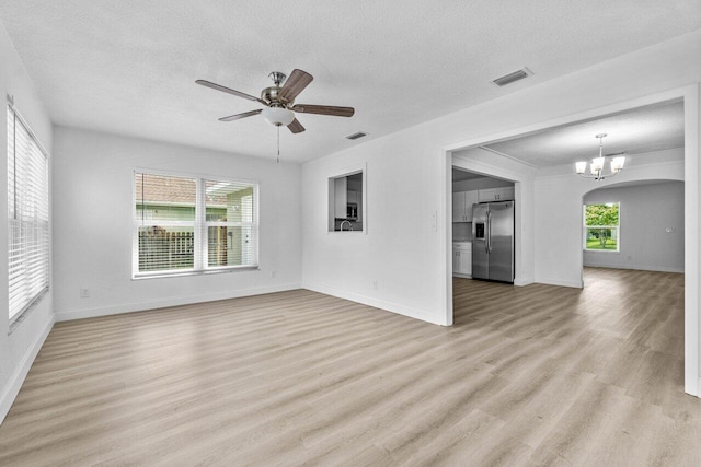 unfurnished living room with a textured ceiling, ceiling fan with notable chandelier, light hardwood / wood-style floors, and a wealth of natural light