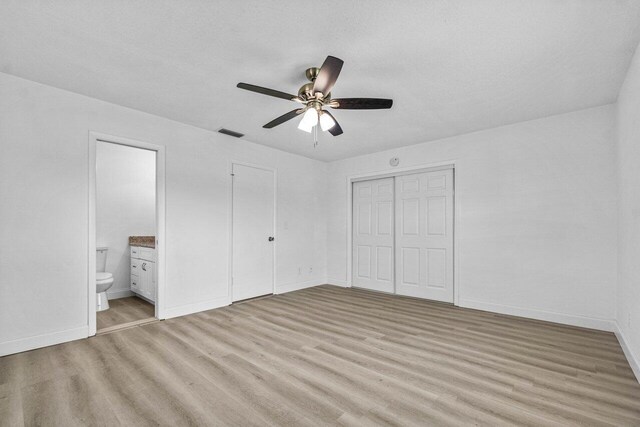 unfurnished bedroom with a textured ceiling, light hardwood / wood-style floors, ensuite bath, and ceiling fan