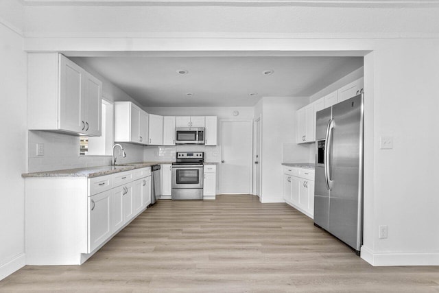 kitchen featuring light wood-type flooring, sink, white cabinets, decorative backsplash, and stainless steel appliances