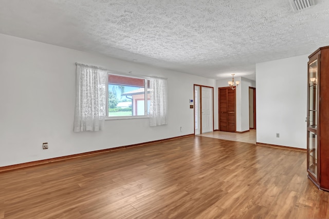 unfurnished room featuring a textured ceiling, light hardwood / wood-style floors, and an inviting chandelier