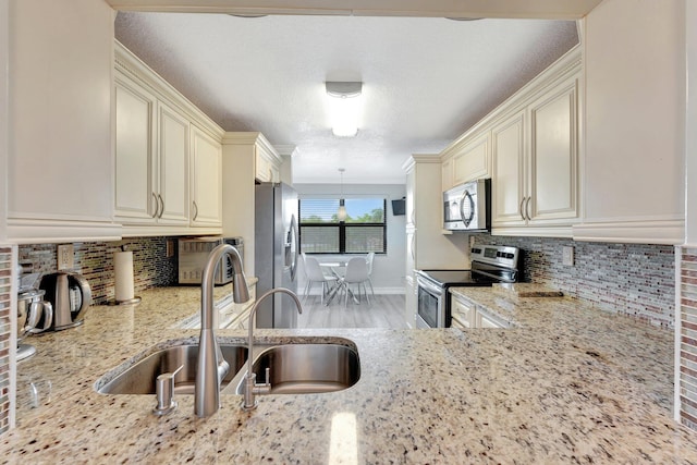 kitchen featuring appliances with stainless steel finishes, light stone countertops, pendant lighting, cream cabinets, and sink