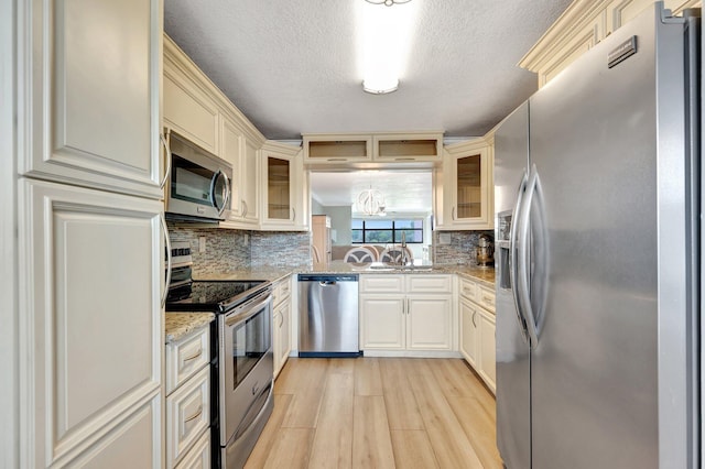 kitchen featuring light stone counters, sink, a textured ceiling, light hardwood / wood-style flooring, and appliances with stainless steel finishes