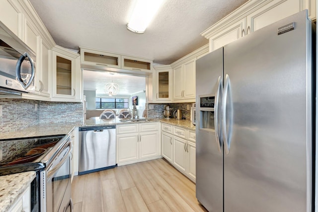 kitchen featuring tasteful backsplash, a textured ceiling, appliances with stainless steel finishes, light stone countertops, and light hardwood / wood-style floors