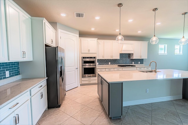 kitchen with a kitchen island with sink, custom range hood, stainless steel appliances, sink, and pendant lighting