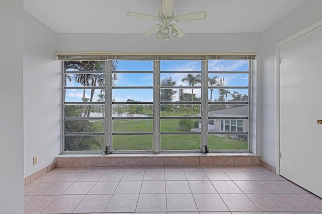 interior space featuring light tile patterned floors, a textured ceiling, a water view, and ceiling fan