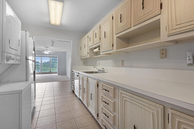 kitchen with sink, ceiling fan, light tile patterned floors, a textured ceiling, and stacked washer / dryer