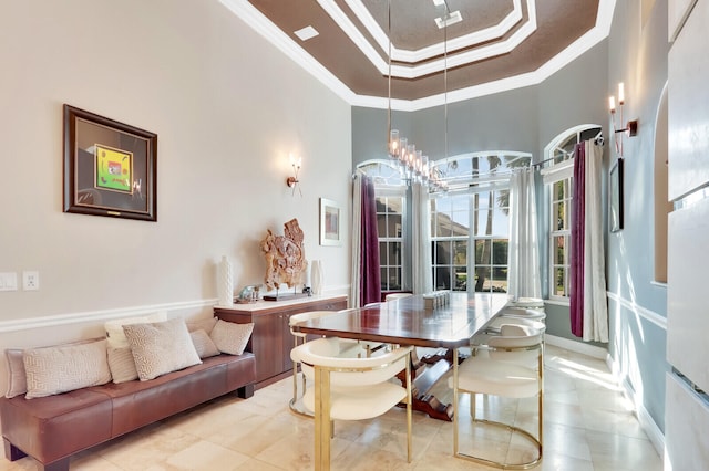 dining room with ornamental molding, a towering ceiling, a raised ceiling, and an inviting chandelier