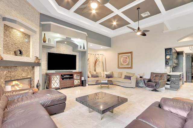 living room featuring coffered ceiling, a towering ceiling, beamed ceiling, a large fireplace, and ceiling fan