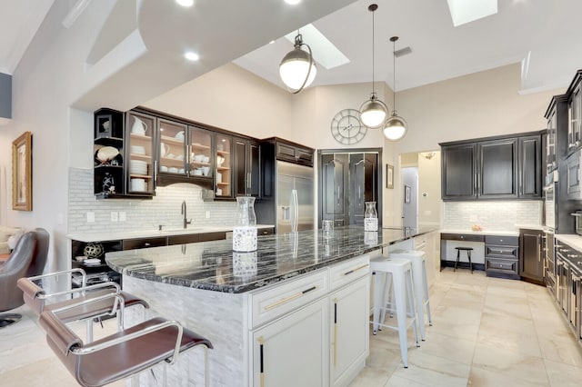 kitchen featuring a center island, a kitchen bar, stainless steel built in fridge, a skylight, and dark stone countertops