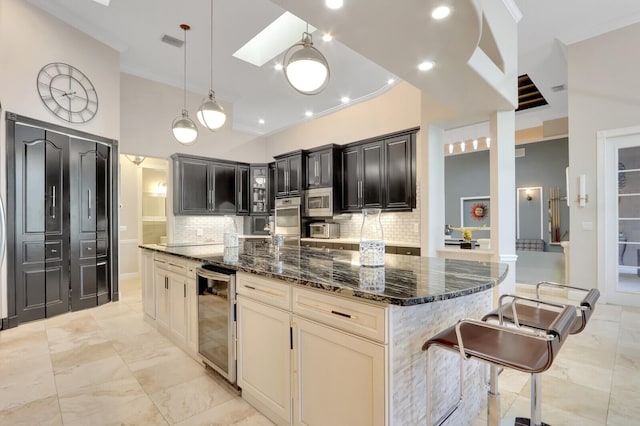 kitchen featuring cream cabinetry, dark stone countertops, a kitchen island, beverage cooler, and a skylight