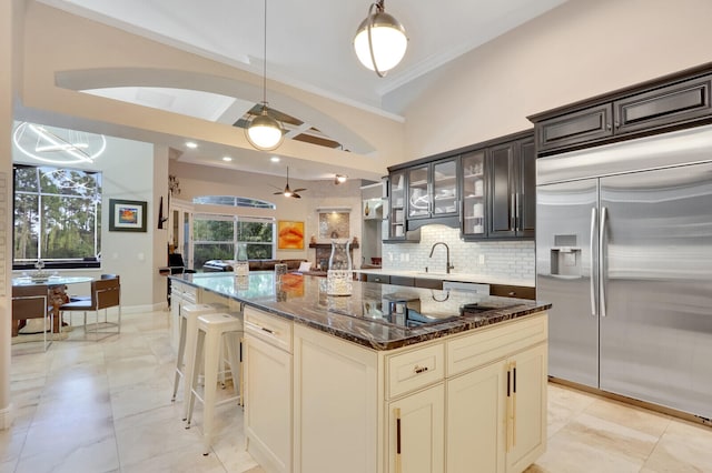 kitchen featuring a kitchen island, built in fridge, crown molding, dark stone countertops, and cream cabinets