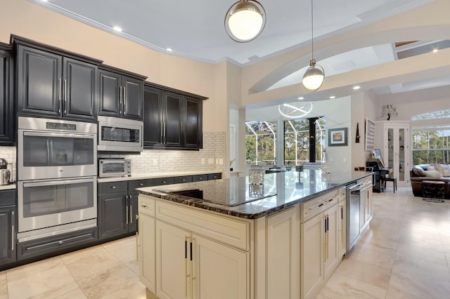 kitchen with dark stone counters, tasteful backsplash, appliances with stainless steel finishes, crown molding, and cream cabinets