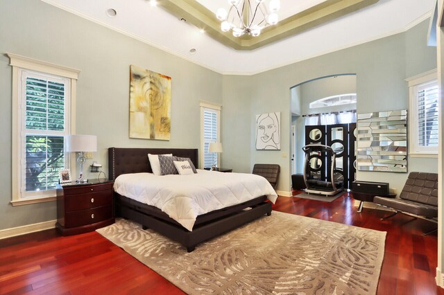 bedroom with an inviting chandelier, a tray ceiling, crown molding, and dark wood-type flooring