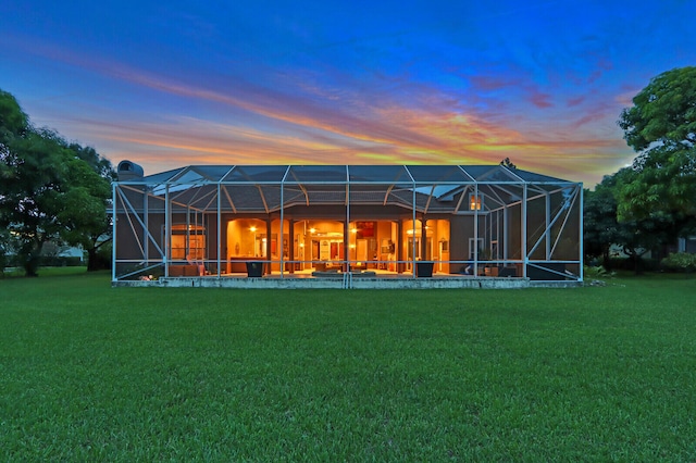 back house at dusk with a yard and glass enclosure