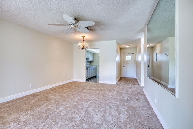 carpeted empty room featuring ceiling fan with notable chandelier and a textured ceiling