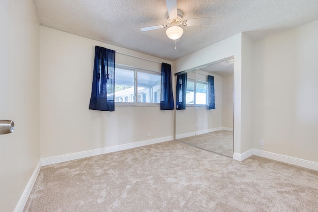 unfurnished bedroom with a closet, a textured ceiling, light colored carpet, and ceiling fan