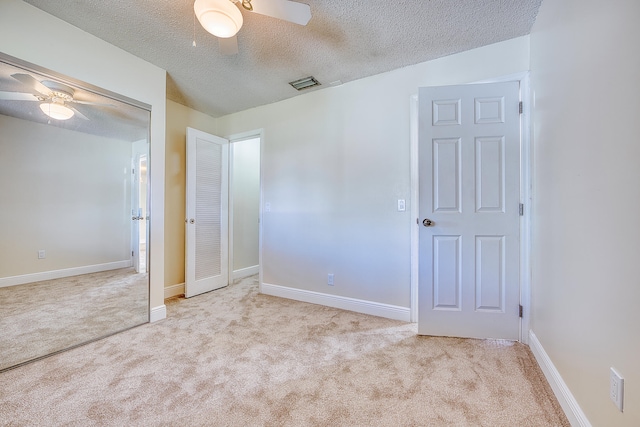 unfurnished bedroom with a closet, a textured ceiling, light colored carpet, and ceiling fan