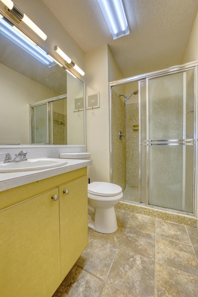 bathroom with vanity, a textured ceiling, toilet, and a shower with door