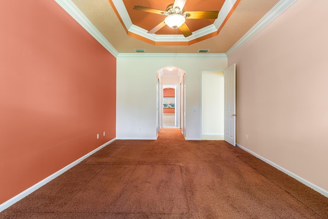 spare room with a tray ceiling, carpet floors, arched walkways, ornamental molding, and a ceiling fan
