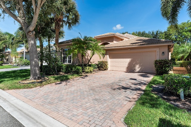 mediterranean / spanish home featuring stucco siding, decorative driveway, a tiled roof, and a garage