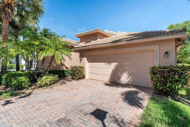 view of front facade featuring a garage, a tile roof, stucco siding, and decorative driveway