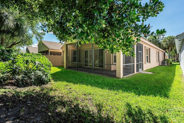 rear view of house with stucco siding, a lawn, and a sunroom