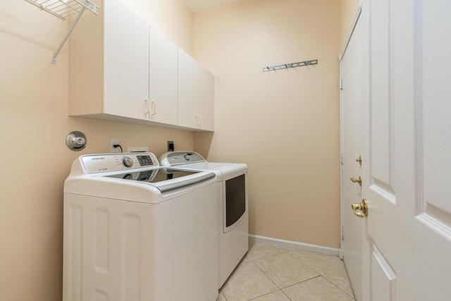 laundry room featuring light tile patterned floors, washing machine and clothes dryer, cabinet space, and baseboards