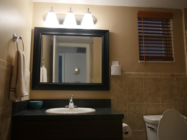 bathroom with tile walls, a textured ceiling, vanity, and toilet