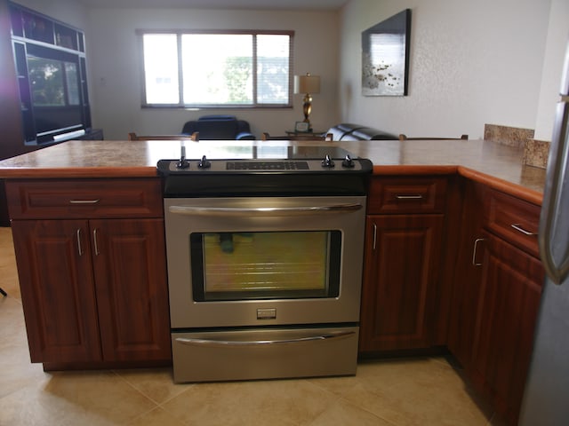 kitchen with kitchen peninsula, stainless steel electric stove, light tile patterned floors, and white refrigerator