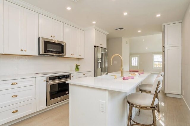 kitchen with white cabinets, light wood-type flooring, an island with sink, appliances with stainless steel finishes, and a breakfast bar area