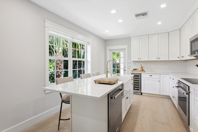 kitchen with white cabinetry, a kitchen island with sink, appliances with stainless steel finishes, and a breakfast bar area