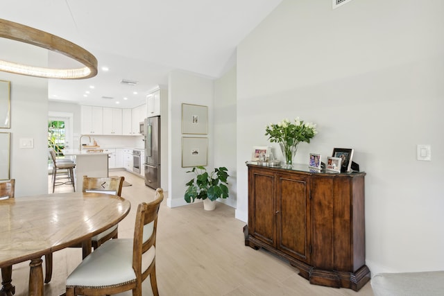 dining room with sink, vaulted ceiling, and light wood-type flooring