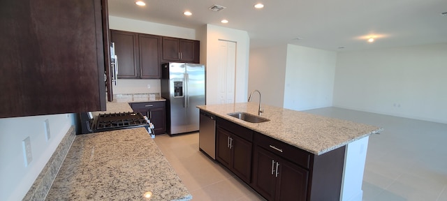 kitchen with light stone counters, an island with sink, light tile patterned flooring, sink, and stainless steel appliances