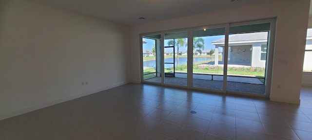 empty room with baseboards, tile patterned flooring, and a water view
