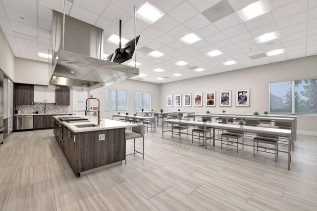 kitchen featuring sink, dark brown cabinets, a large island, a paneled ceiling, and a breakfast bar