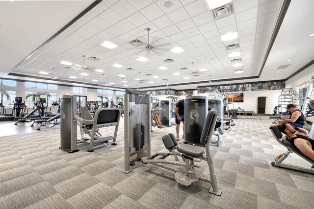 gym featuring light colored carpet, a tray ceiling, and ceiling fan