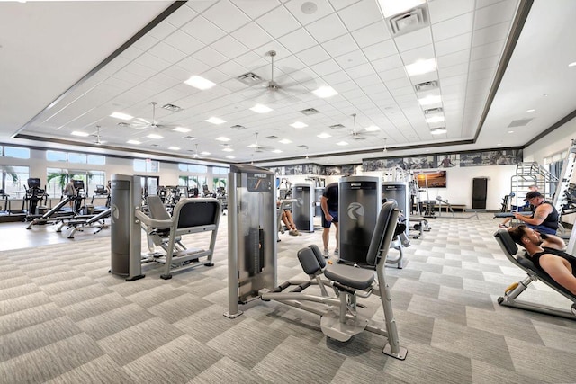 workout area featuring ceiling fan, visible vents, a raised ceiling, and light colored carpet