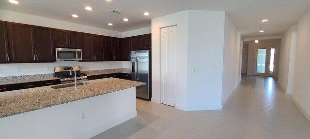 kitchen featuring dark brown cabinets, stainless steel appliances, light stone countertops, and sink