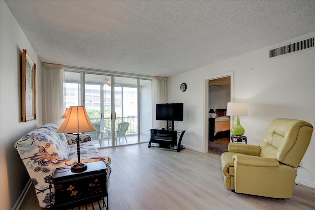 living area with light wood-style floors, visible vents, a wall of windows, and a textured ceiling