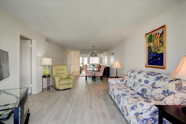 living room featuring light wood-style floors, visible vents, and a textured ceiling