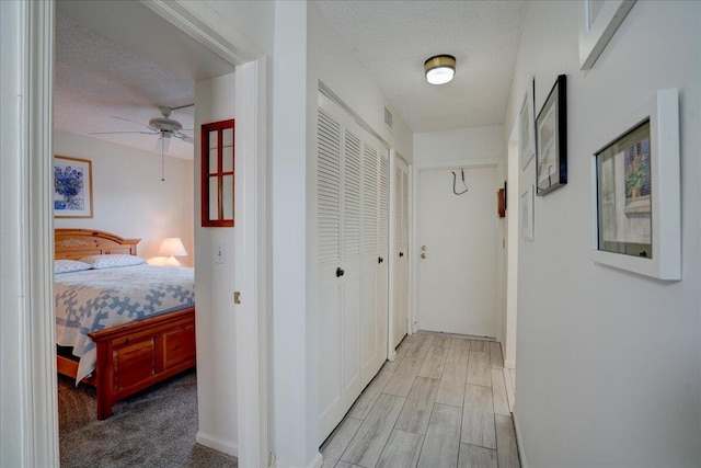 hallway with a textured ceiling, baseboards, visible vents, and wood tiled floor