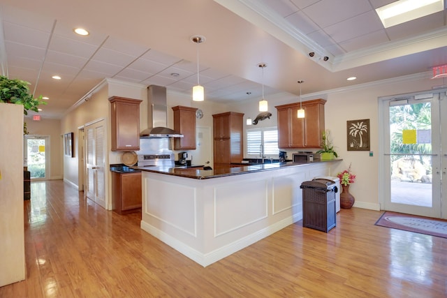 kitchen featuring brown cabinetry, dark countertops, and wall chimney range hood