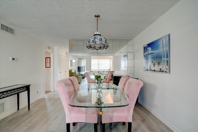 dining space with baseboards, visible vents, a textured ceiling, and light wood finished floors