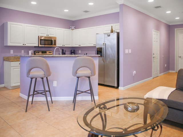 kitchen with a center island with sink, white cabinetry, stainless steel appliances, and a breakfast bar