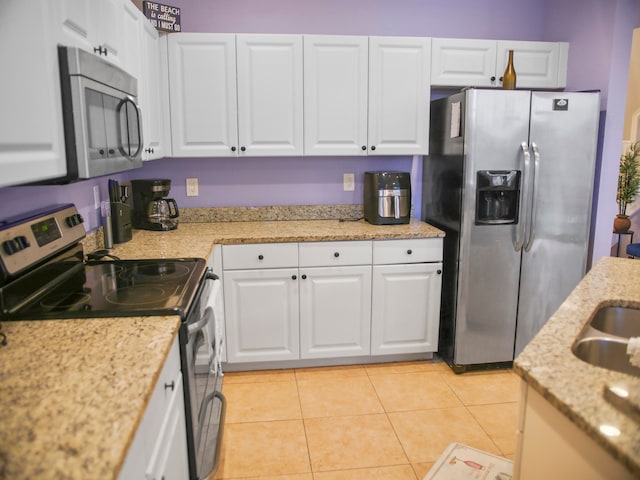 kitchen featuring appliances with stainless steel finishes, white cabinetry, light tile patterned floors, and light stone counters