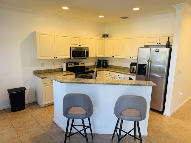 kitchen with stainless steel appliances, white cabinetry, a kitchen breakfast bar, and dark stone counters