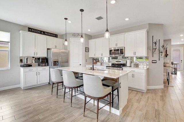 kitchen with a breakfast bar, stainless steel appliances, a center island with sink, and a healthy amount of sunlight